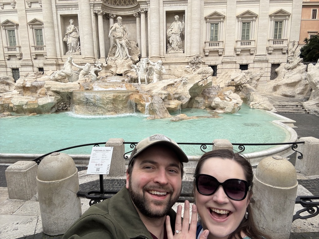 My partner and I at the Trevi Fountain in Rome. We&rsquo;re both smiling, and you can see an engagement ring on her finger